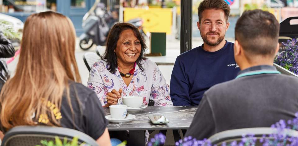 Four people sat around a table outside in Oxford Street drinking coffee and talking