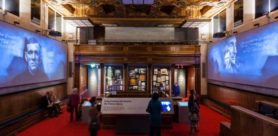 Inside the Titanic Exhibition at Seacity museum with people looking at information boards and screens on either side of the room