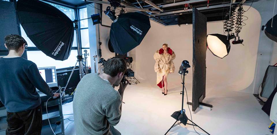 A photoshoot with a fashion model posing in front of cameras and lights with a white background