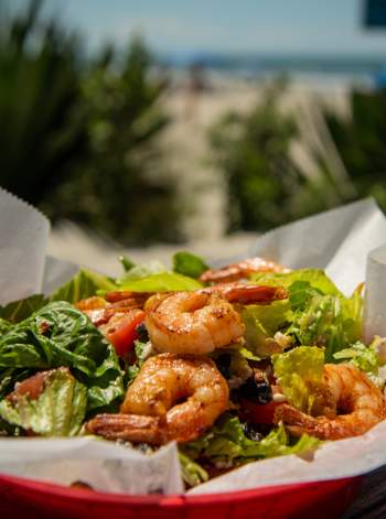 a salad with shrimp in a red basket on a table by the beach