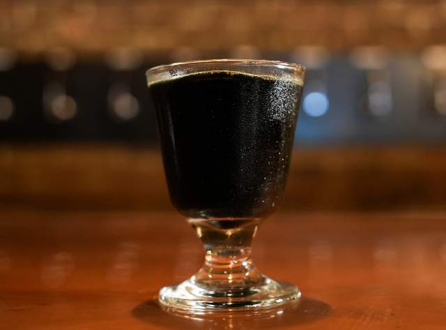 A glass with dark liquid on a bar