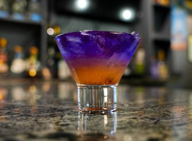 A small rocks glass with purple and orange drink