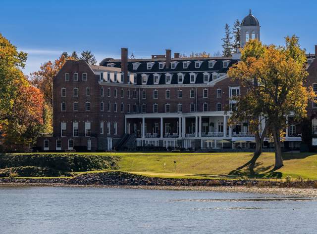 The Otesaga Resort surrounded by trees with autumn foliage, situated beside Otsego Lake