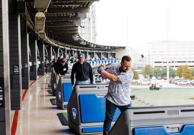 People lined up on their tees, at varying points in their golf swings in the bays at Top Golf.
