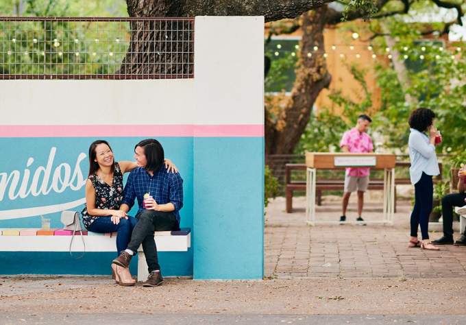 Couple sitting in front of Bienvenidos sign under live oak tree at Fresas outdoor patio in Austin Texas