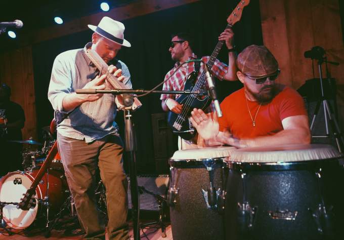 three members of El Tule band play bongo drums bass guitar and traditional wooden instrument at Barracuda for Hot Luck Fest