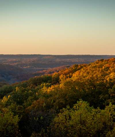 Sunset illuminates rolling forested hills covered in autumn foliage.