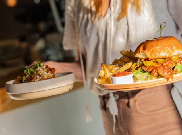 Woman carrying two plates of food - one with a hamburger, the other obscured in the distance
