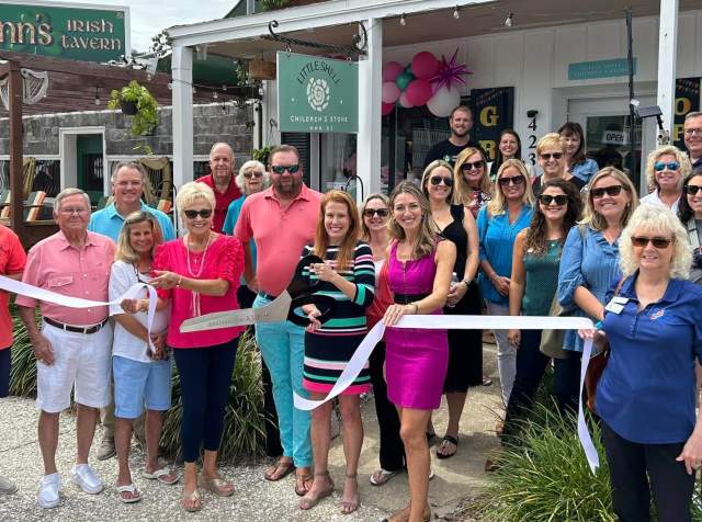 Ribbon cutting ceremony at Little Shell Children's Store on Main Street in North Myrtle Beach, hosted by Destination NMB. Community members, local business owners, and Destination North Myrtle Beach representatives celebrate the grand opening in front of the store, next to Flynn's Irish Tavern