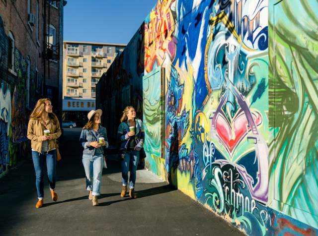 3 girls walking in sunlit alley with murals