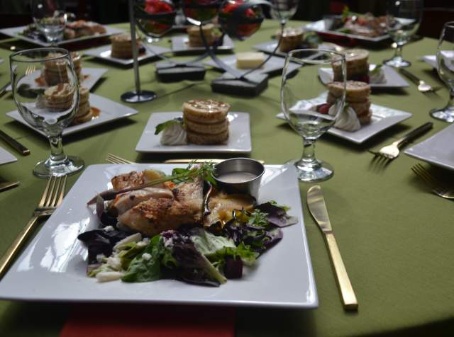 Chicken salad on square plates set on a green table cloth with utensils and dessert