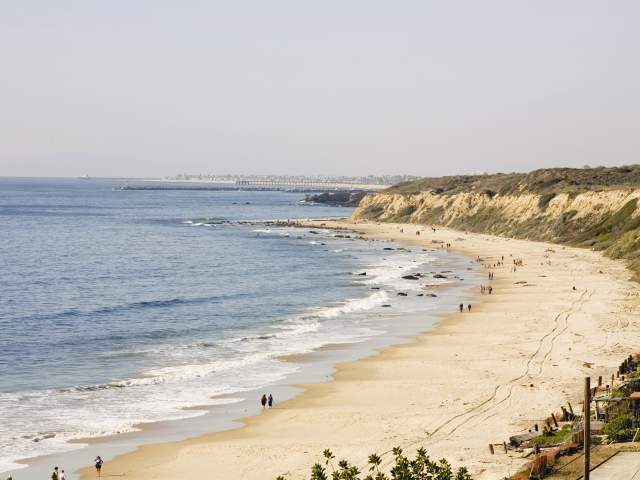 Emerald Vista Point at Crystal Cove State Park in Orange County, California, featuring a scenic coastal overlook with sandy beaches, gentle ocean waves, rugged bluffs, and visitors walking along the shoreline beneath a clear sky.