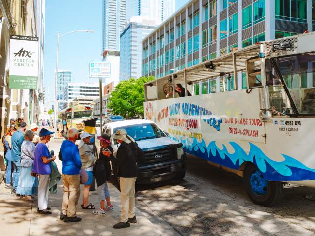 People line up on the sidewalk outside of the Austin Visitor Center waiting to board the Duck Tour vehicle