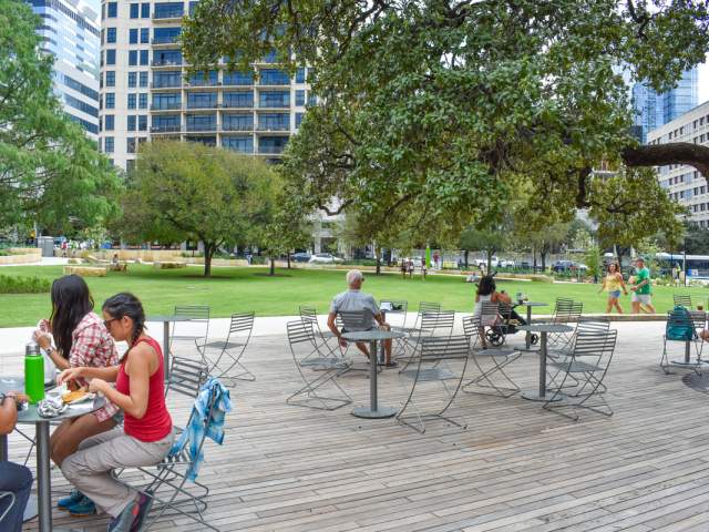 Groups of people sitting at bistro tables on a wooded deck next to an expansive park.