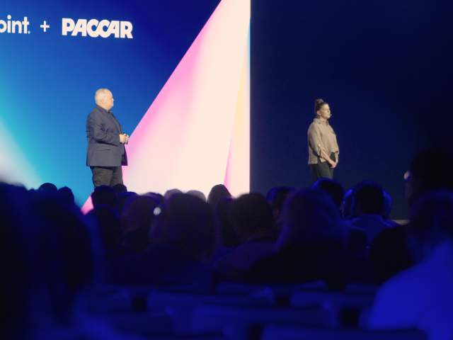 Two executives speaking in front of a room of hundreds of attendees.