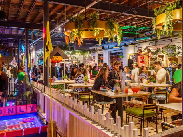 People sitting at bartop tables enjoying food and drink in the colorfully lit Holey Moley Golf Club.