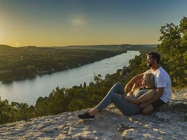 Couple lounging atop Mount Bonnell at sunset, overlooking Lake Austin