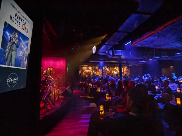 Parker Jazz Club with seats filled with people at candle lit tables while the Paker House Band plays on stage.