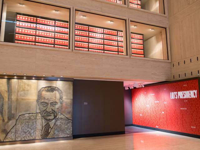 Interior atrium of the LBJ Presidential Library, showcasing archives, a stone mural of President LBJ and a preview of the hallway exhibit that outlines his presidential legacy.
