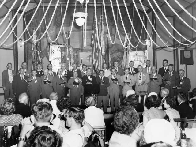 Historic black and white photo of a mens chorus performing at Saengerrunde Hall