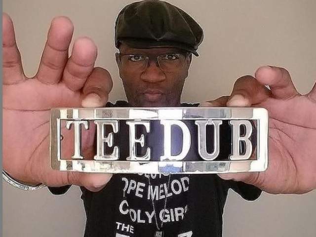 Tee Double holds silver sign saying TEE DUB towards camera