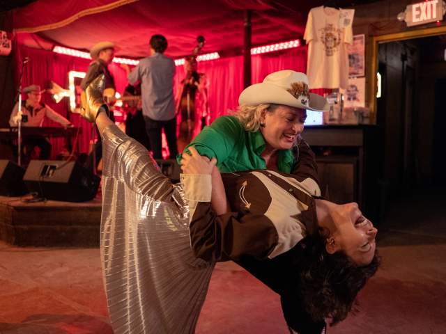 Two women in Western attire country dancing in a dance hall.