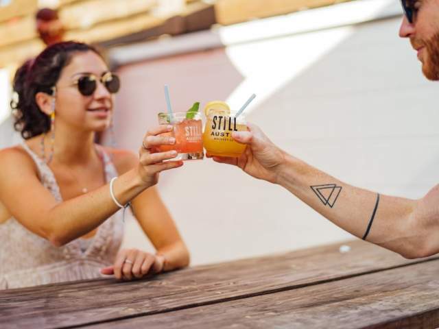 Image of a man and women holding their cocktails together on the patio at Still Austin Whiskey Co.