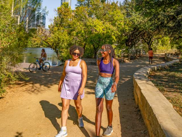 Two women walking along the sunny Hike-and-Bike trail along Lady Bird Lake.