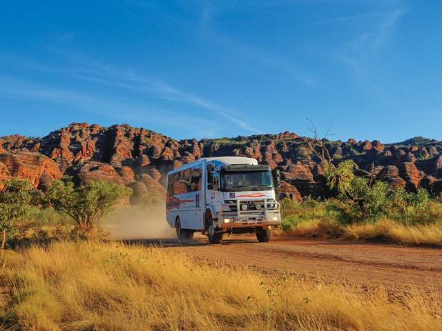 An APT Kimberley tour vehicle in Purnululu National Park shown with the striped domes of the Bungle Bungle Ranges in the background
