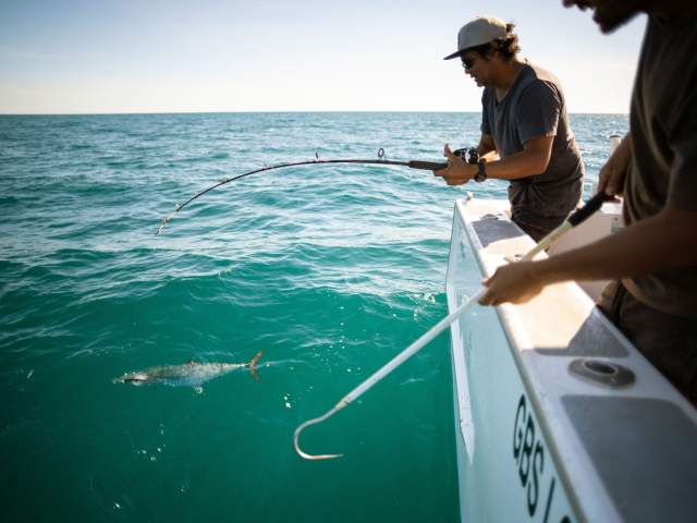 A man catching a fish from a charter boat at Lombadina Community on the Dampier Peninsula; another man is ready to pull the fish on board.
