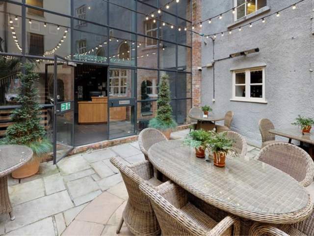 An ourdoor patio with tables and chairs in front of a large glass windows and doors - Credit Hotel Du Vin