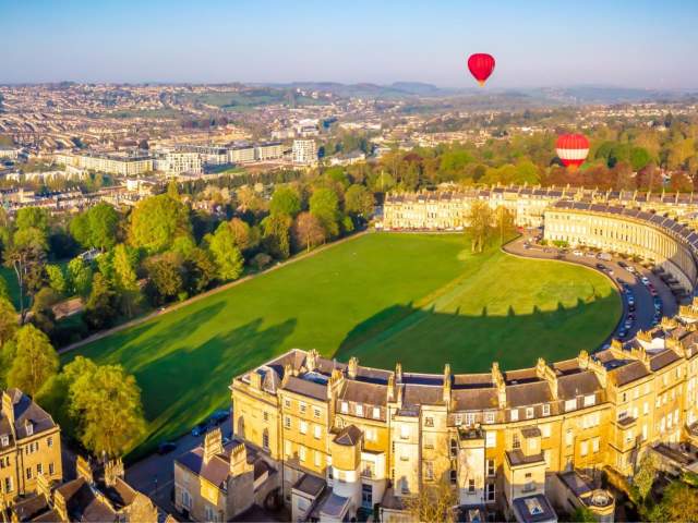 An aerial view of the Royal Crescent in Bath near Bristol, with hot air balloons launching from the green