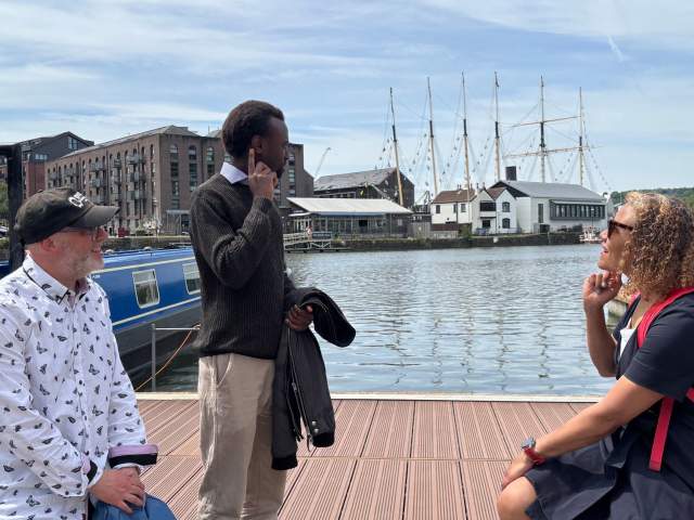 3 people sat on decking next to Bristol Harbour