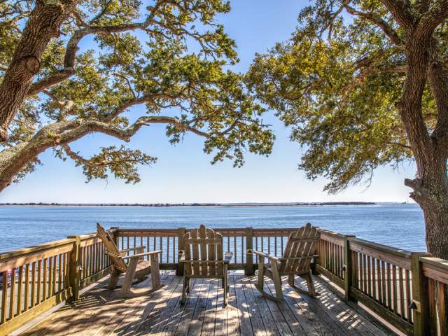 A wooden deck with three chairs overlooking water with trees on both sides