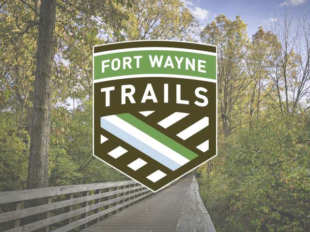 Fort Wayne Trails logo overlaid on a picture of a Rivergreenways trail in the fall