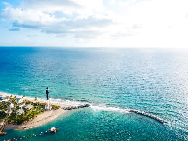 The Hillsboro Lighthouse stands at the edge of the Hillsboro Inlet, surrounded by the crystal blue Florida coastline