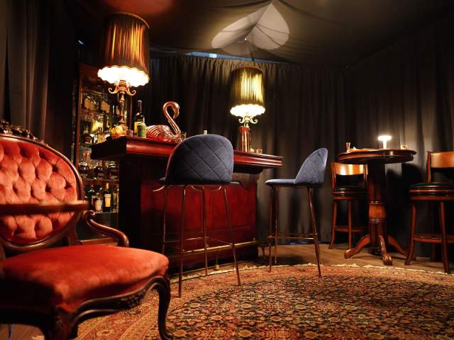 Inside of Room 901, plush velvet chair in front of a mahogany colored private bar.