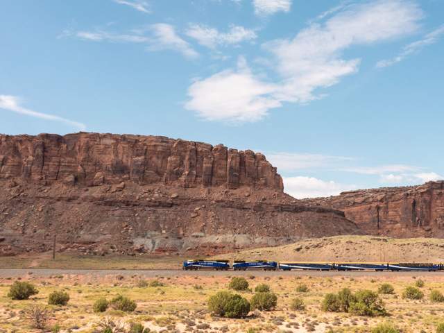 An Amtrak train traversing the desert with Moab’s red rock in the background.