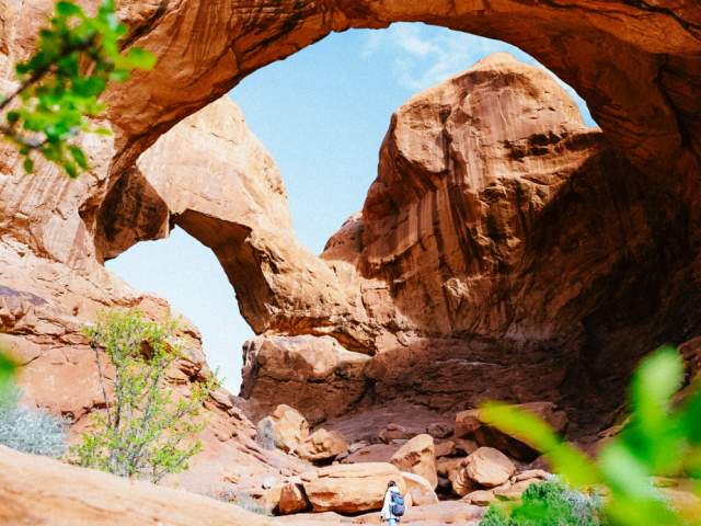 A hiker walks under Double Arch, one of the most famous and massive natural sandstone formations in Arches National Park, Utah.