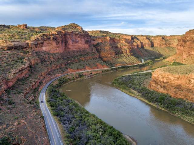 An aerial view of the Upper Colorado River Scenic Byway (Utah State Route 128) winding alongside the Colorado River through a dramatic red rock canyon near Moab, Utah.