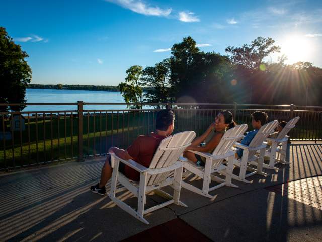 A family sitting in white rocking chairs enjoying the view of Lake James at Pokagon State Park.