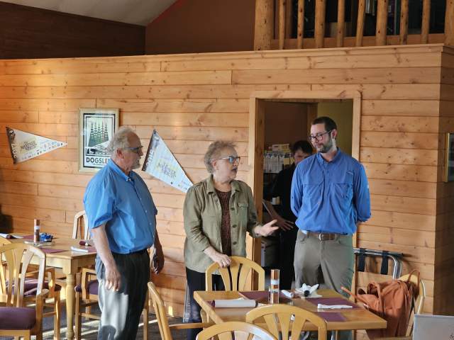 3 figures speak together congenially in a lodge-like restaurant setting