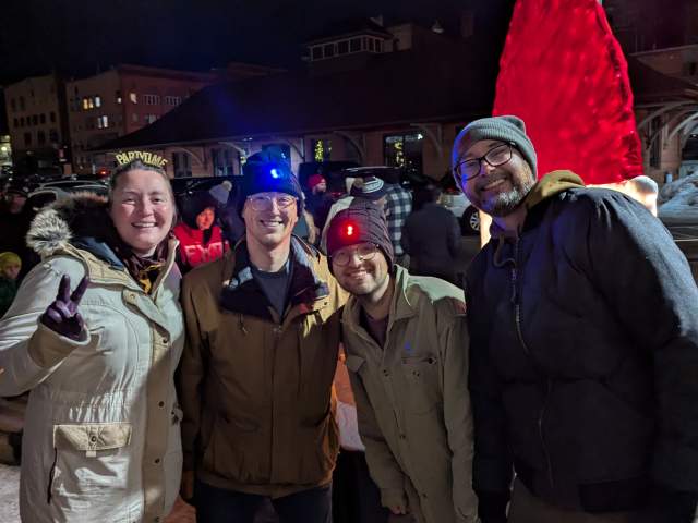 four people stand smiling outdoors at night