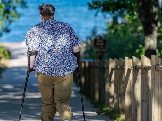 a figure using mobility aids walks down a ramp towards a lake