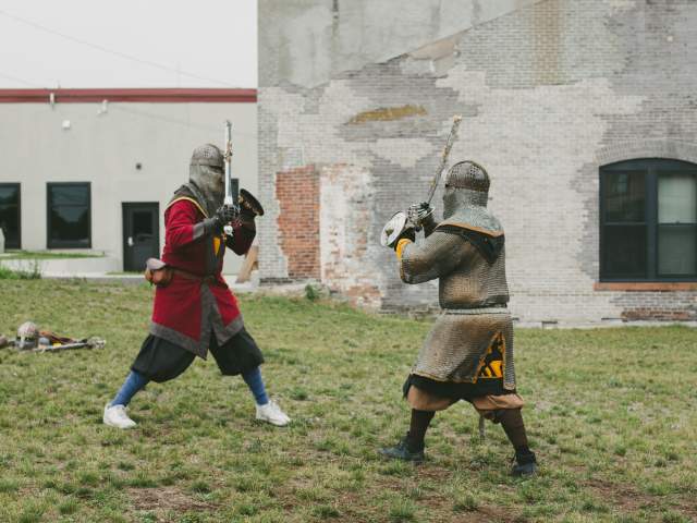 two figures costumed in medieval garb mock fight with swords