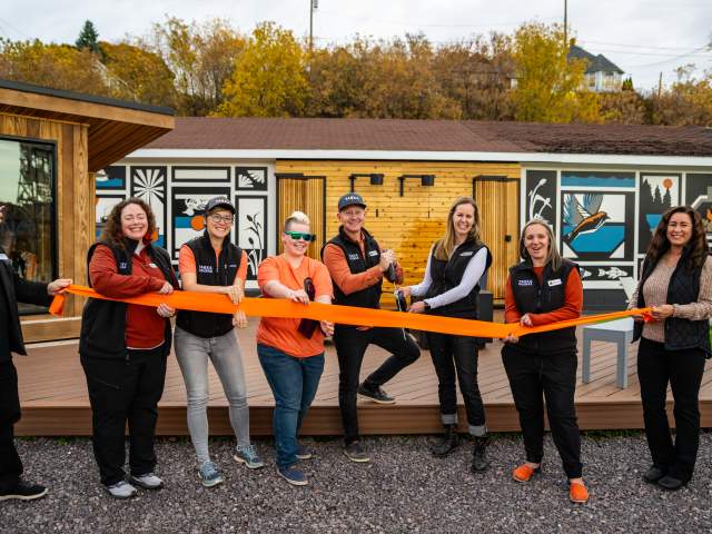 people smile while holding a ribbon in front of a wooden sauna