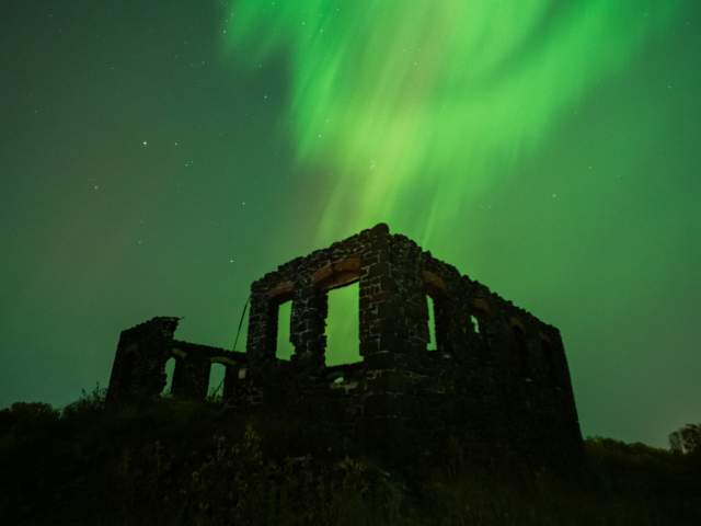 northern lights paint the sky with a ruin in dark silhouette in the foreground