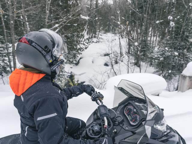a helmeted snowmobiler pauses on the trail looking into woods