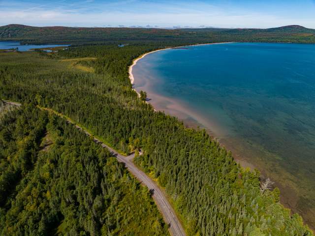 a rural highway road runs through a dense forest along a bay