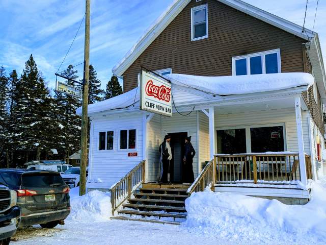two people stand on the porch of a snow laden small town bar